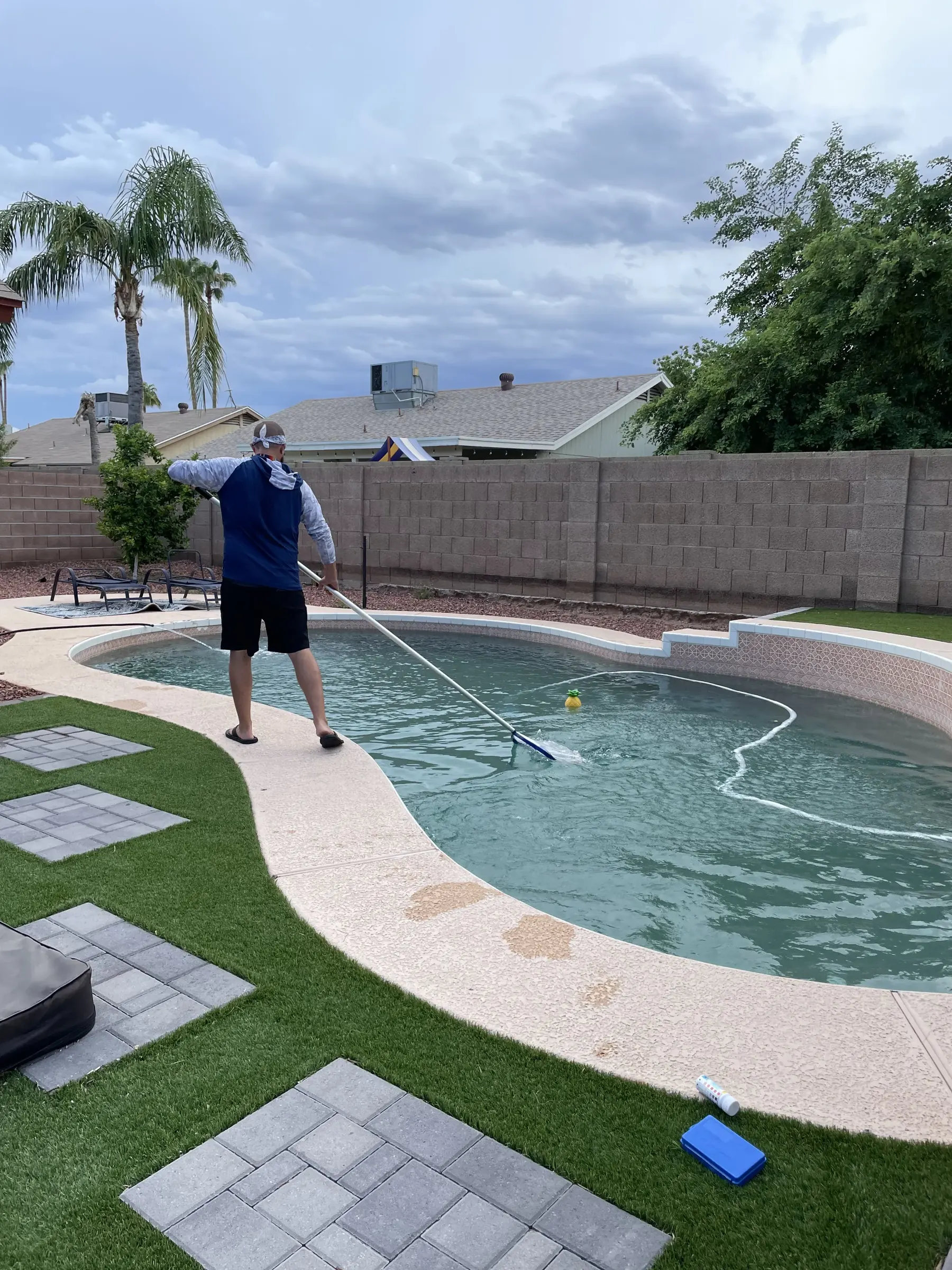 DJ from Bell Road Pool Care skimming a backyard pool in Phoenix
